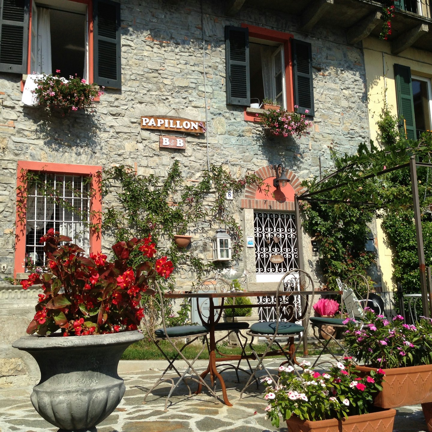 Bed and breakfast in pietra con mobili da giardino e vasi di fiori.